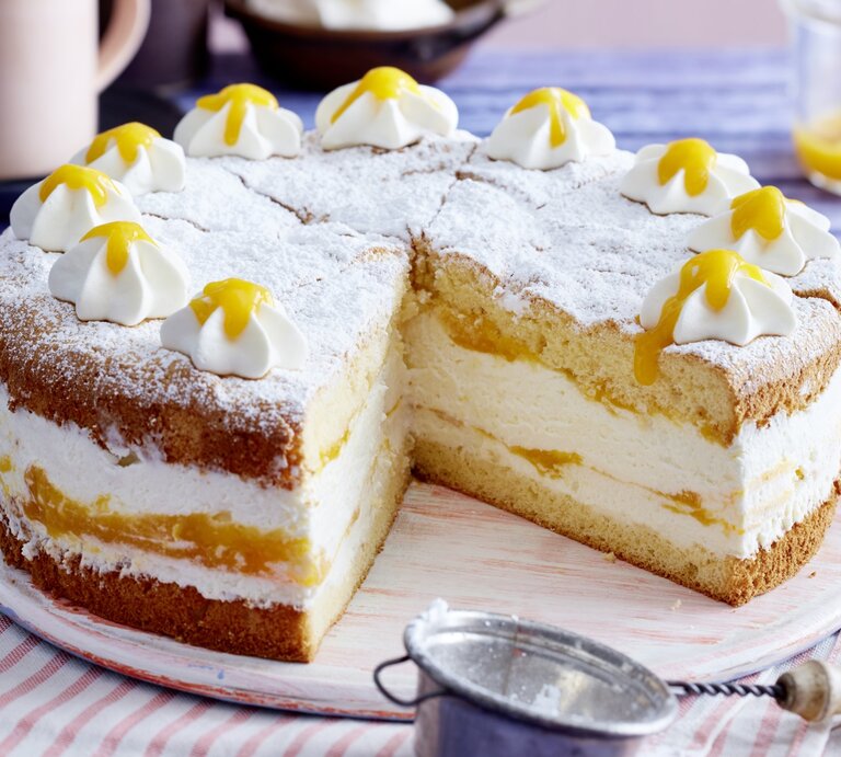 Auf einem Holzteller steht eine Quark-Mangotorte. Sie ist mit Puderzucker und Sahnetuffs verziert. | © EAT CLUB / Isabell Triemer