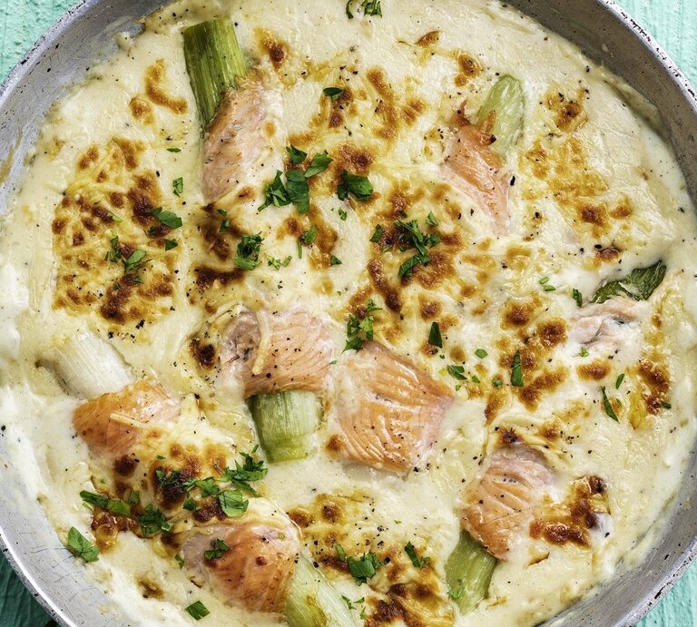 In einer Auflaufform ist ein gratinierter Lachs mit Lauch, Käsesauce und Kartoffelpüree angerichtet. Er ist mit Käse überbacken.  | © StockFood / [PhotoCuisine]