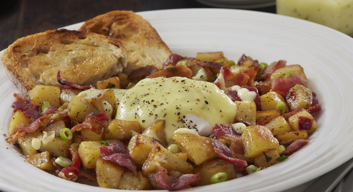 Bauernfrühstück mit Speck und Kartoffeln, pochiertem Ei und Sauce hollandaise auf einem weißen Teller. 