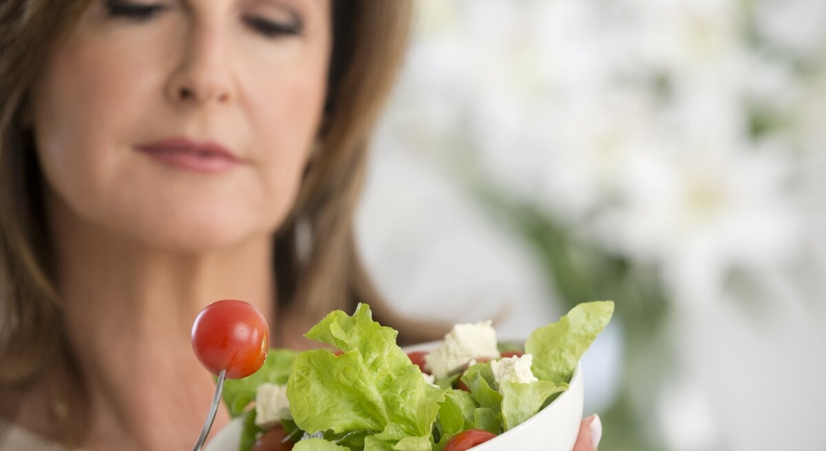 Frau mit einer Salatschale in der Hand beäugt kritisch eine kleine Tomate. 