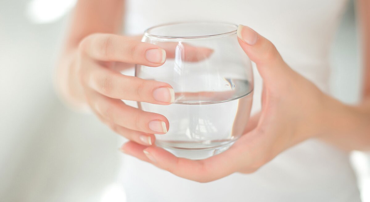 Frau hält Glas Wasser in den Händen. Insbesondere auf die Ernährung vor einer Darm- oder Magenspiegelung sollten Sie achten.