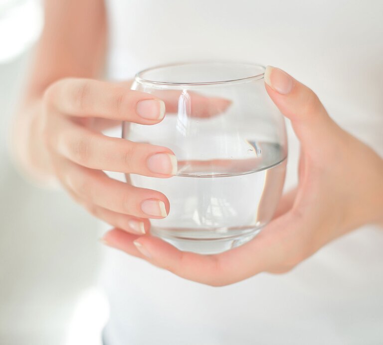 Frau hält Glas Wasser in den Händen. Insbesondere auf die Ernährung vor einer Darm- oder Magenspiegelung sollten Sie achten. | © Shutterstock/VBStudio