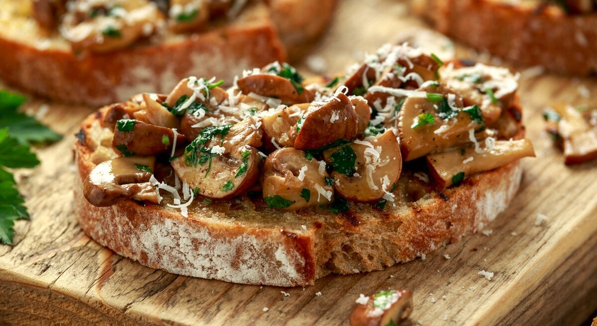 Eine Pilzstulle mit Knoblauchfrischkäse und Parmesan auf einem Holzbrett.