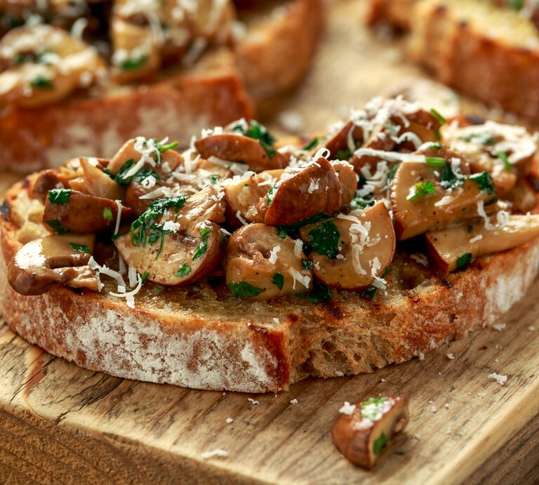 Eine Pilzstulle mit Knoblauchfrischkäse und Parmesan auf einem Holzbrett. | © Getty Images/ 	DronG
