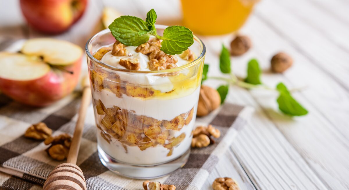 Herbst-Dessert im Glas mit Apfel, Walnuss, Quark und Honig auf hellem Holz.