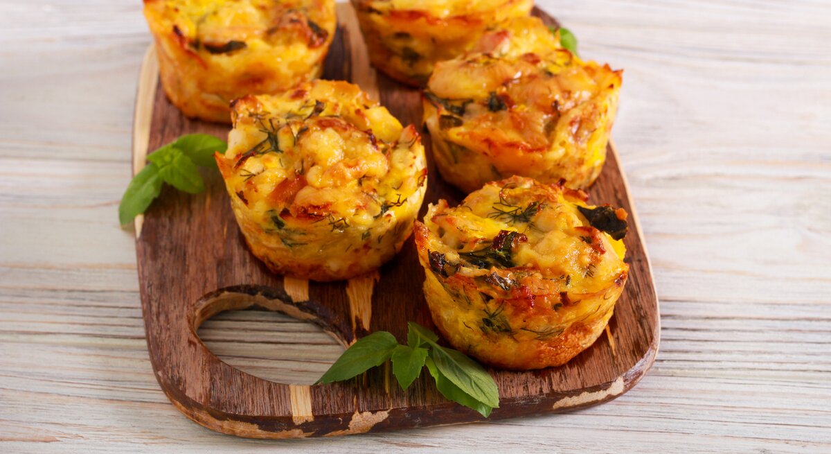 Ein Brett mit herzhaften Kartoffelmuffins mit Käse überbacken, daneben einige Petersilienblätter.