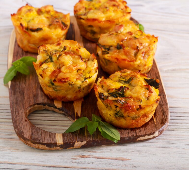 Ein Brett mit herzhaften Kartoffelmuffins mit Käse überbacken, daneben einige Petersilienblätter. | © Getty Images/ manyakotic