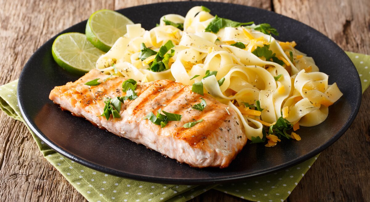 Ein schwarzer Teller mit Pasta mit Lachs und Cheddar auf einem rustikalen Holztisch.