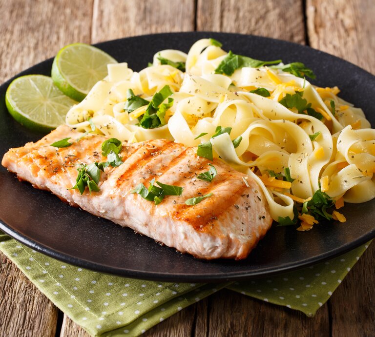 Ein schwarzer Teller mit Pasta mit Lachs und Cheddar auf einem rustikalen Holztisch. | © Shutterstock/AS Foodstudio