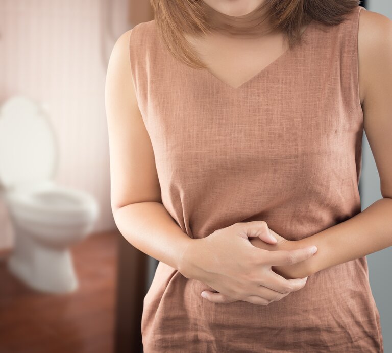 Frau hat eine Blasenentzündung und hält sich den Bauch. Im Hintergrund sieht man das Badezimmer und die Toilette.  | © Getty Images/Tharakorn Arunothai / EyeEm
