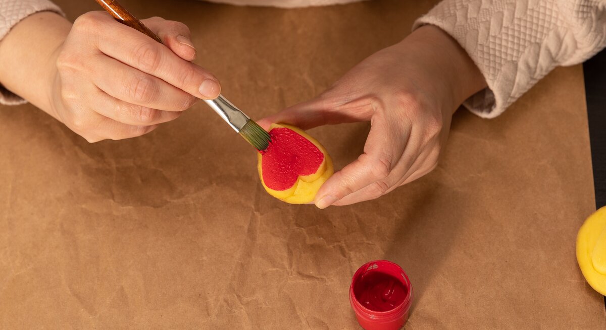 Eine Frau bemalt mit roter Farbe einen herzförmigen Kartoffelstempel.