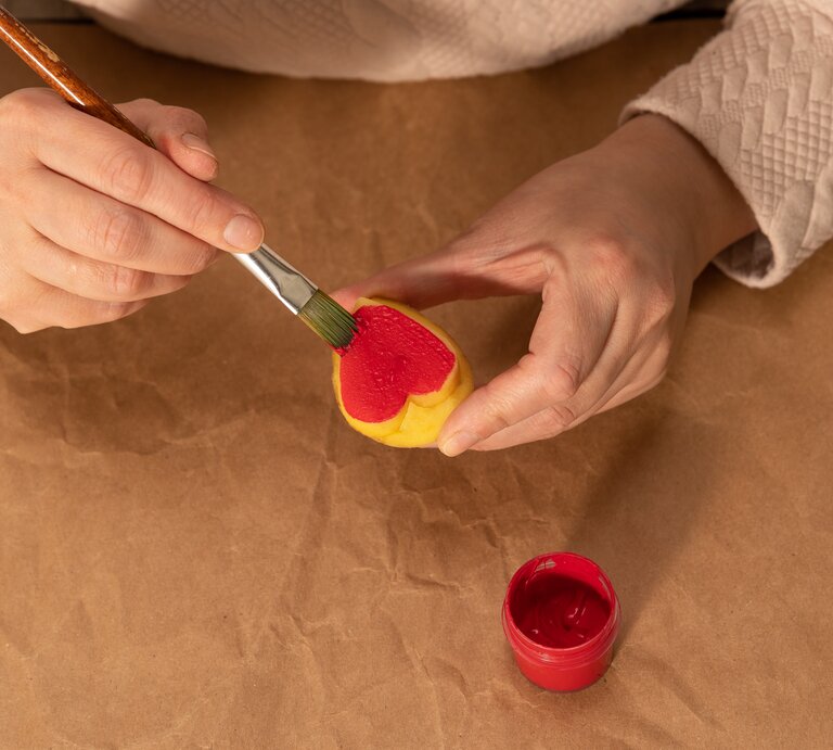 Eine Frau bemalt mit roter Farbe einen herzförmigen Kartoffelstempel. | © Shutterstock/Alas_spb