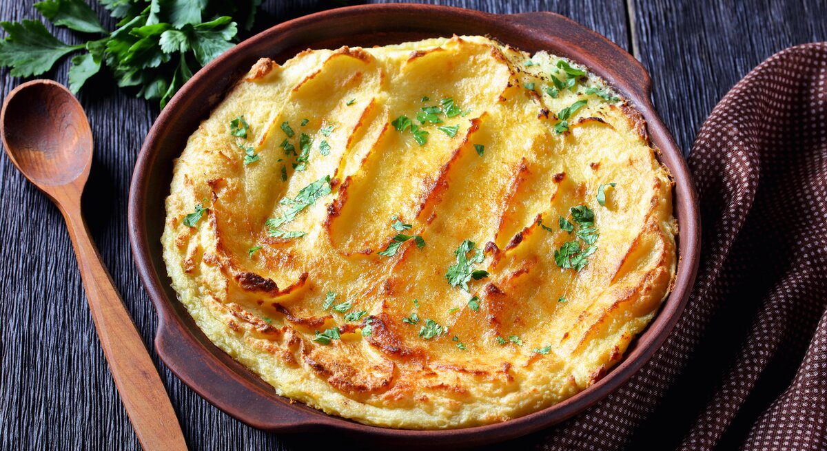 Schale mit gebackenem Kartoffelpüree auf dunklem Untergrund.