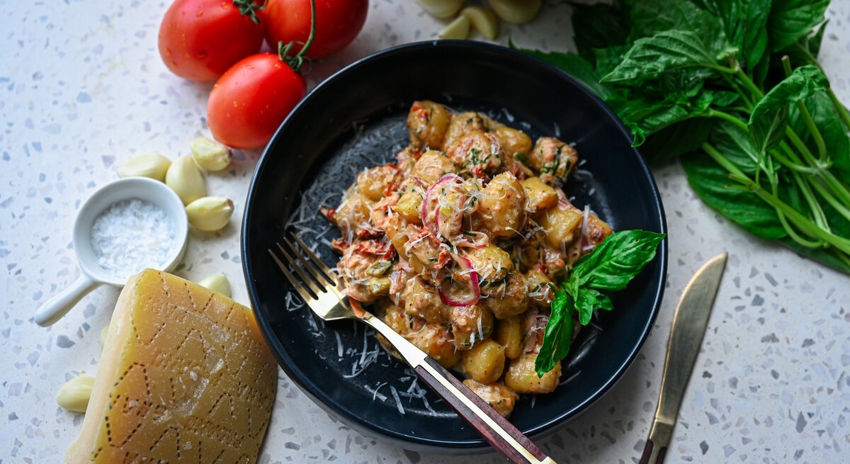 Schnitzeltopf mit Gnocchi auf schwarzem Teller – darum herum liegen einige der Zutaten verteilt.