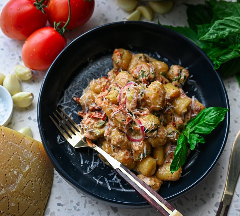 Schnitzeltopf mit Gnocchi auf schwarzem Teller – darum herum liegen einige der Zutaten verteilt. | © AdobeStock/arekor