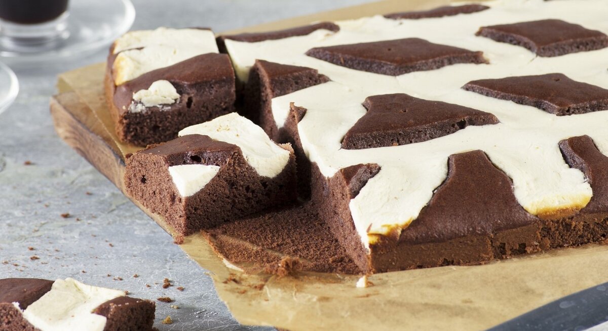 Auf einem Backpapier liegt ein Kuhflecken-Kuchen. Er hat ein geflecktes Muster aus Schokolade und Vanille.