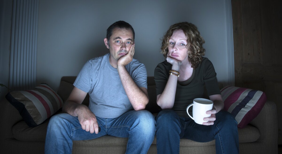 Ein Paar sitzt gelangweilt auf der Couch und schaut fern.