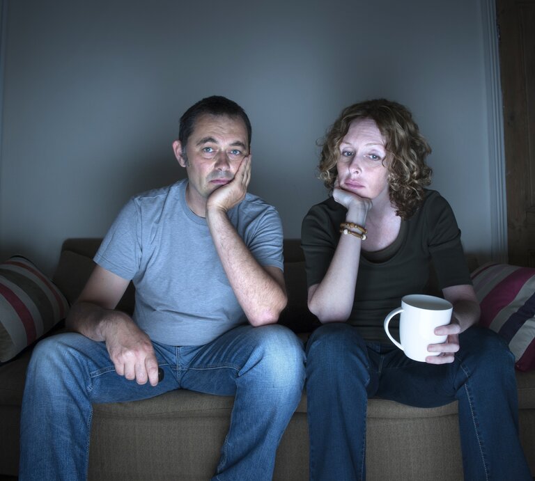 Ein Paar sitzt gelangweilt auf der Couch und schaut fern. | © iStock.com/eelnosiva