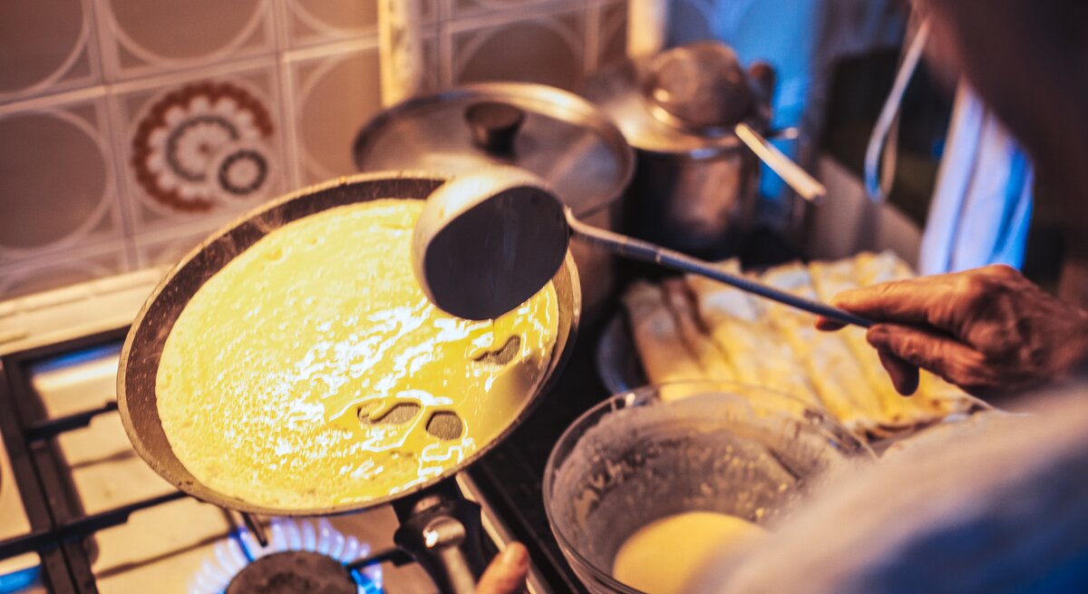 Ältere Frau bereitet Pfannkuchen in einer altmodischen Küche zu. 