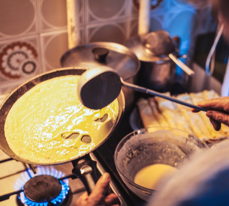Ältere Frau bereitet Pfannkuchen in einer altmodischen Küche zu.  | © Getty Images/ CasarsaGuru
