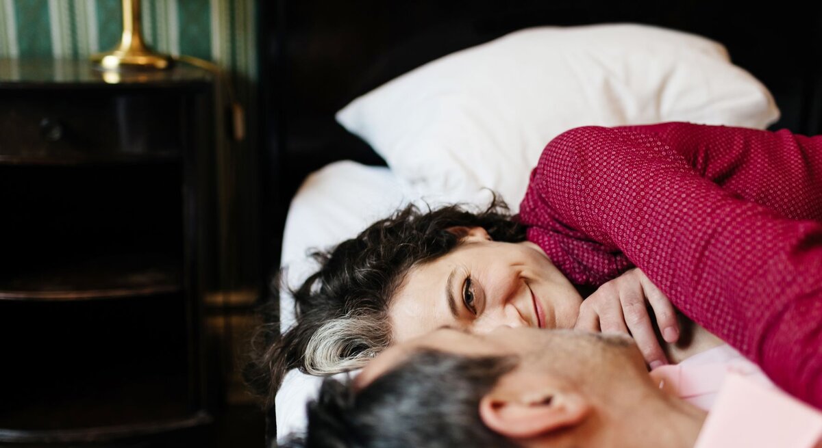 Paar liegt auf Bett und schaut sich verliebt an.