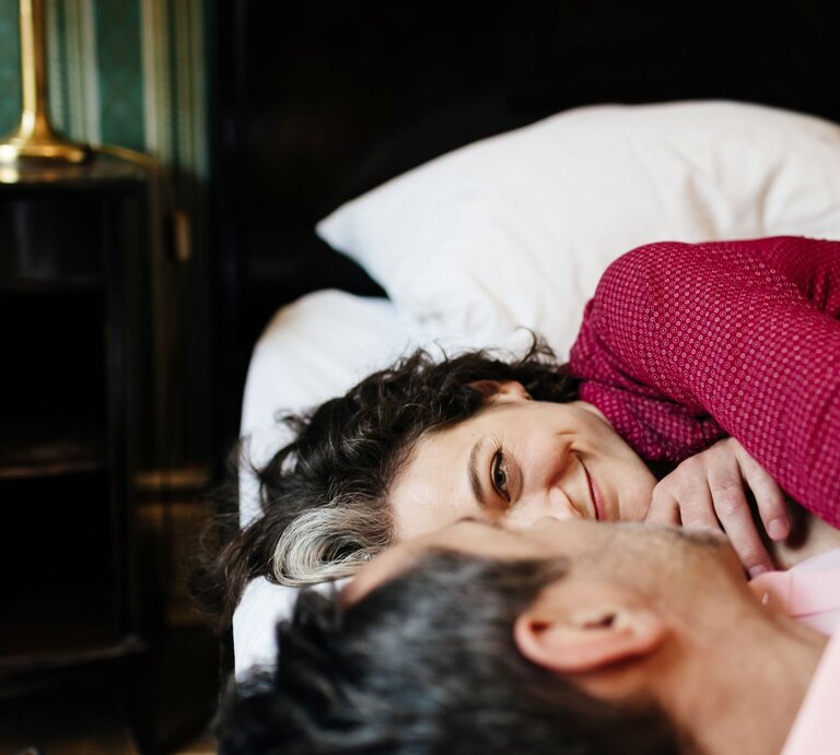 Paar liegt auf Bett und schaut sich verliebt an. | © Getty Images / Hinterhaus Productions