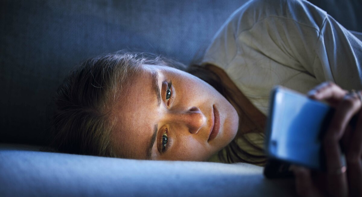 Frau liegt im Bett und starrt auf ihr Handy.