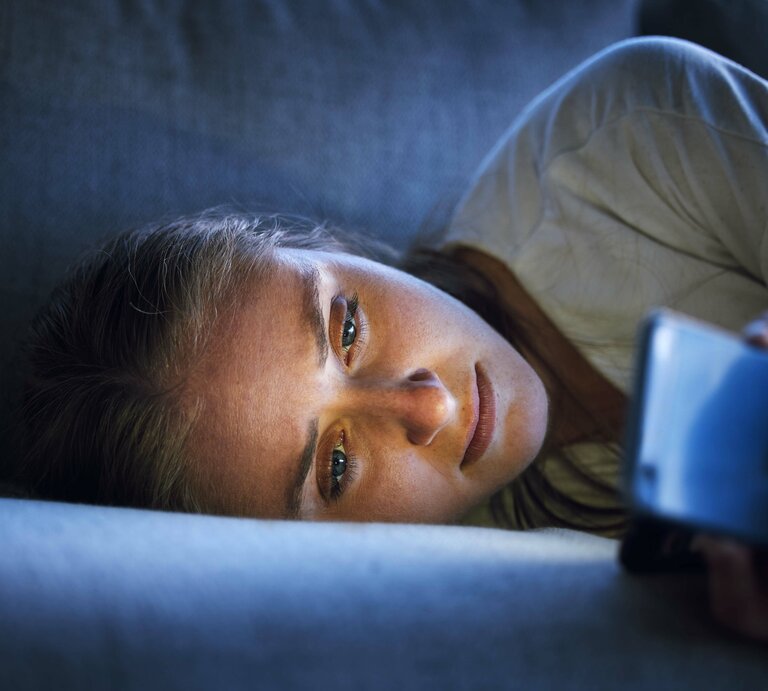 Frau liegt im Bett und starrt auf ihr Handy. | © 
IMAGO / Zoonar