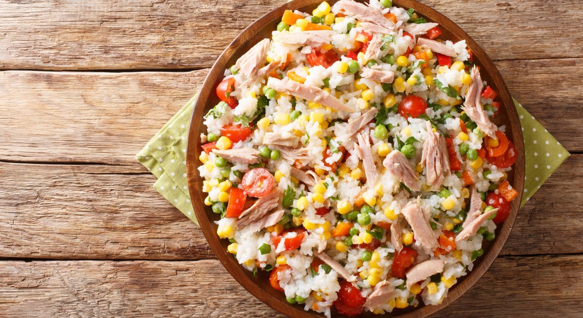 Reissalat mit Thunfisch und Gemüse in brauner Tonschale auf Papierserviette auf Holztisch. Aufnahme aus der Vogelperspektive.