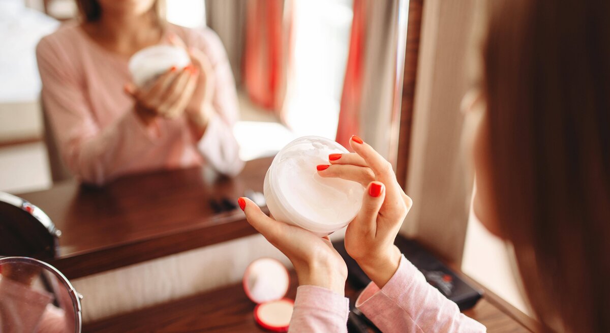 Close-up einer Frau, die mit ihren Fingern Creme aus einer Cremedose nimmt. 