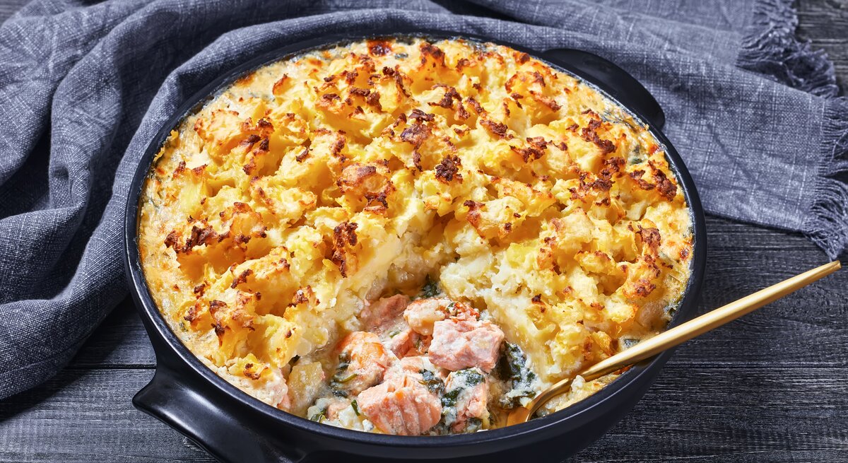 Gusseiserner Topf mit dem Gratin auf grauem Tisch mit grauer Tischdecke.