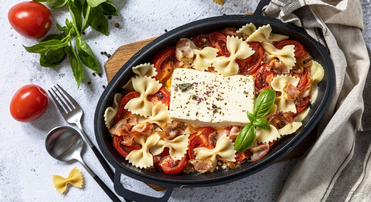 Eine schwarze Auflaufform mit der Feta-Pasta mit Speck auf grauem Untergrund.