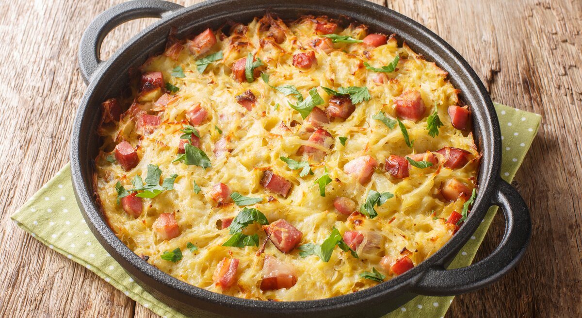 Pfannenrösti mit Speck und Lauch in gusseiserner Pfanne auf Holztisch. 