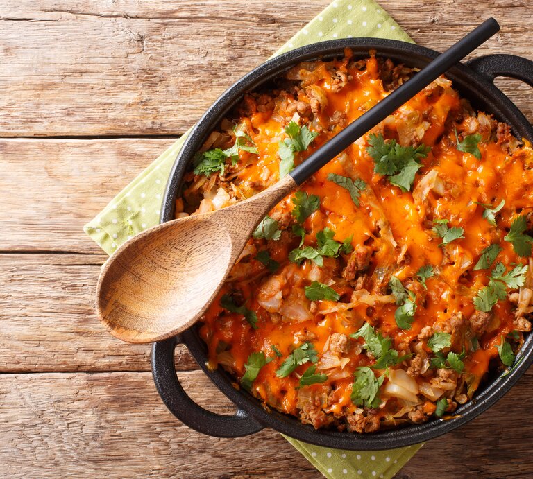 Kohlauflauf mit Hackfleisch und Cheddar in gusseiserner Pfanne auf Holztisch.  | © GettyImages/ALLEKO
