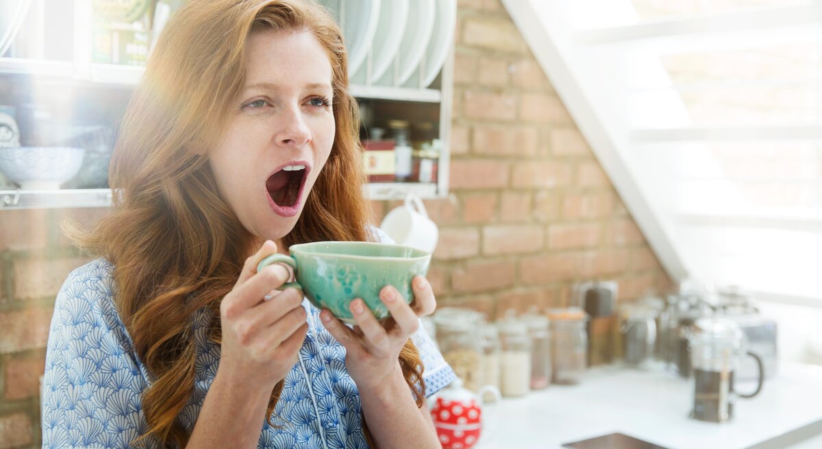 Frau gähnt mit großer Tasse in der Hand