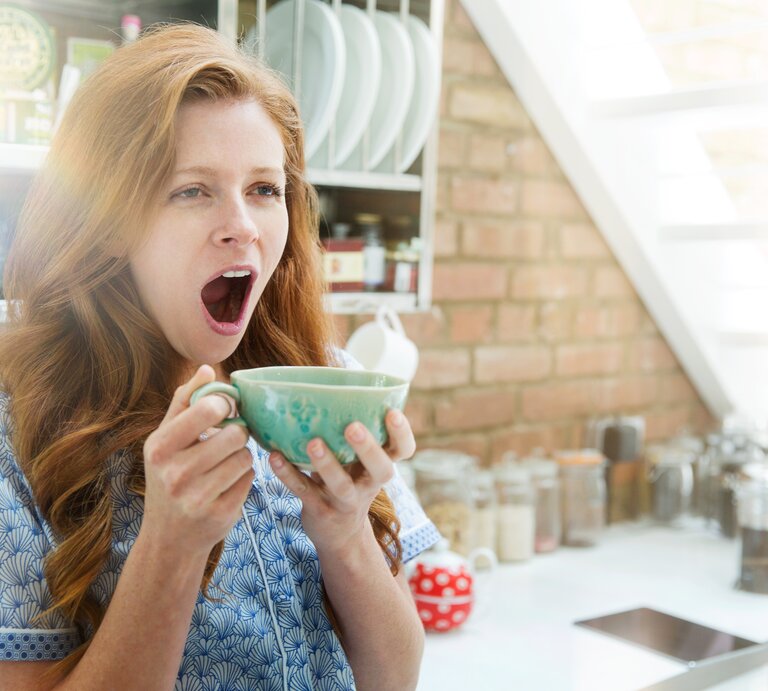 Frau gähnt mit großer Tasse in der Hand | © Getty Images/Tim Robberts