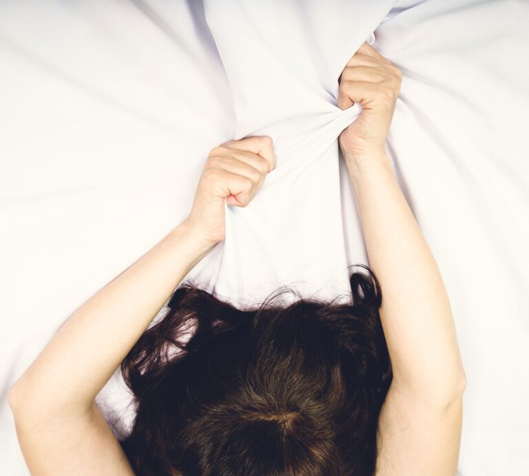 Arme von Frau im Bett, die sie erregt in die Höhe streckt | © Shutterstock / volkovslava