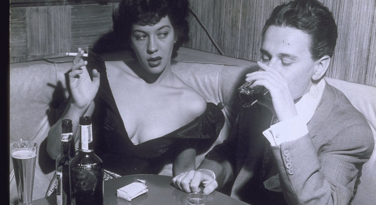 Ein Mann und eine Frau sitzen am Ecktisch einer Bar und trinken und rauchen.