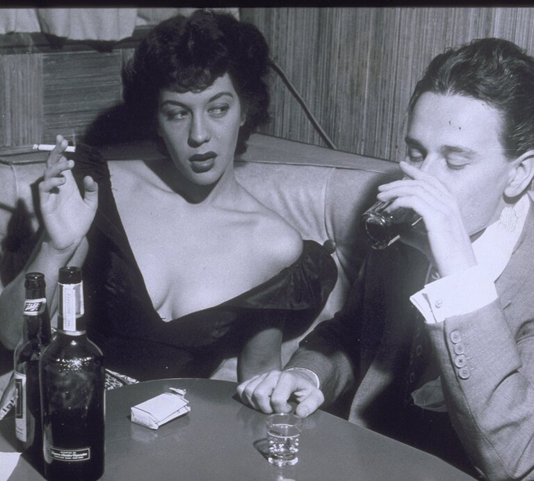 Ein Mann und eine Frau sitzen am Ecktisch einer Bar und trinken und rauchen. | © Archive Holdings Inc. via GettyImages