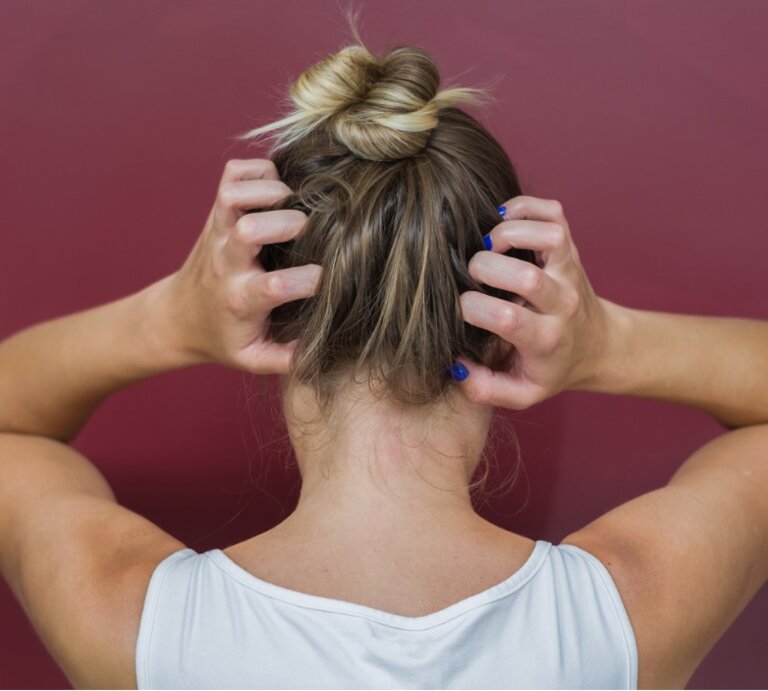Rückansicht einer Frau, die sich mit beiden Händen an den Kopf fasst. Sie trägt ein weißes Tanktop und hat ihr blondes Haar zu einem lässigen Dutt hochgesteckt. Ihre Fingernägel sind blau lackiert. Der Hintergrund ist einheitlich weinrot, was einen Kontrast zu ihrer hellen Kleidung und Haarfarbe bildet. | © istock.com / Thiago Santos