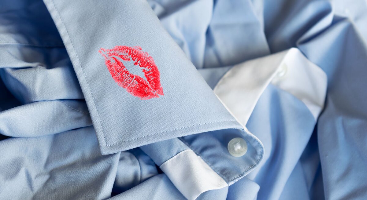 Auf der Manschette eines Herrenhemdes ist ein auffälliger roter Lippenstiftabdruck zu sehen. Der Abdruck hebt sich deutlich von dem hellen Stoff ab