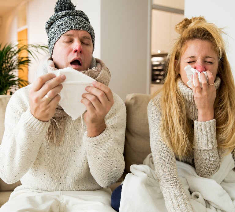 Ein Paar sitzt erkältet auf dem Sofa. Mann und Frau niesen und husten. Die Leute haben eine Erkältung und eine laufende Nase.  | © shutterstock/Aleksandra Suzi