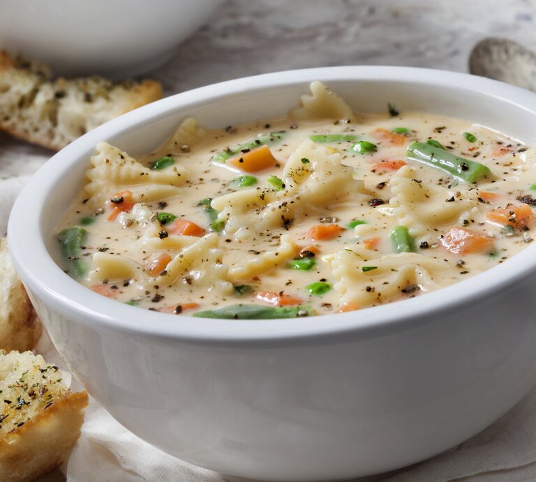 Suppenteller gefüllt mit Käse-Nudelsuppe mit Gemüse auf hellem Untergrund. | © Getty Images/LauriPatterson
