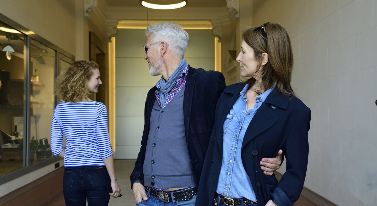 Ein reiferes Paar, Arm in Arm, der Mann schaut einer anderen Frau hinterher