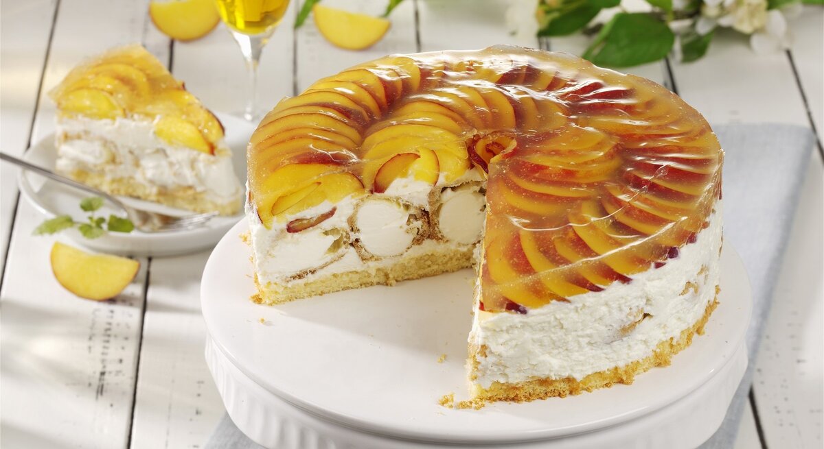 Auf einem Teller ist eine Windbeutel-Schmand-Torte mit Pfirsichen angerichtet. Sie ist mit Windbeuteln gefüllt.
