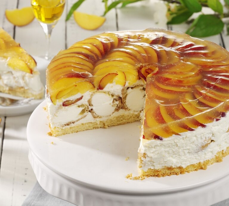 Auf einem Teller ist eine Windbeutel-Schmand-Torte mit Pfirsichen angerichtet. Sie ist mit Windbeuteln gefüllt. | © StockFood / StockFood Studios / Photoart
