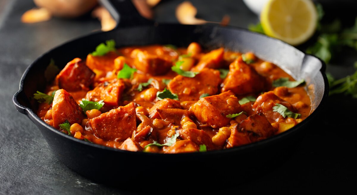 Eine dunkle Pfanne mit Tikka Masala mit Süßkartoffeln und Kichererbsen bestreut mit frischem Koriander.