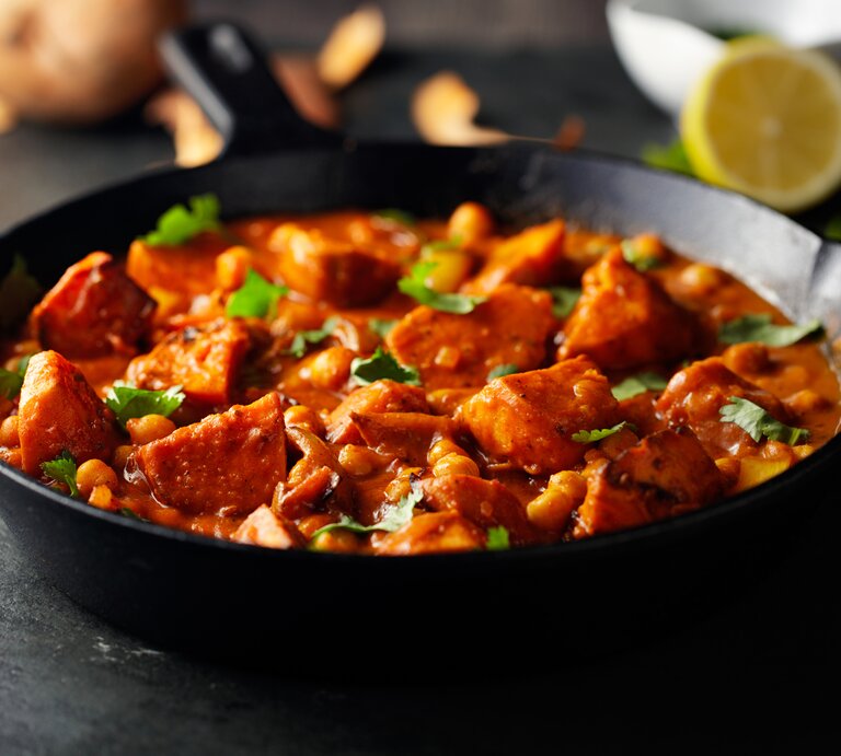 Eine dunkle Pfanne mit Tikka Masala mit Süßkartoffeln und Kichererbsen bestreut mit frischem Koriander. | © Getty Images/ haoliang