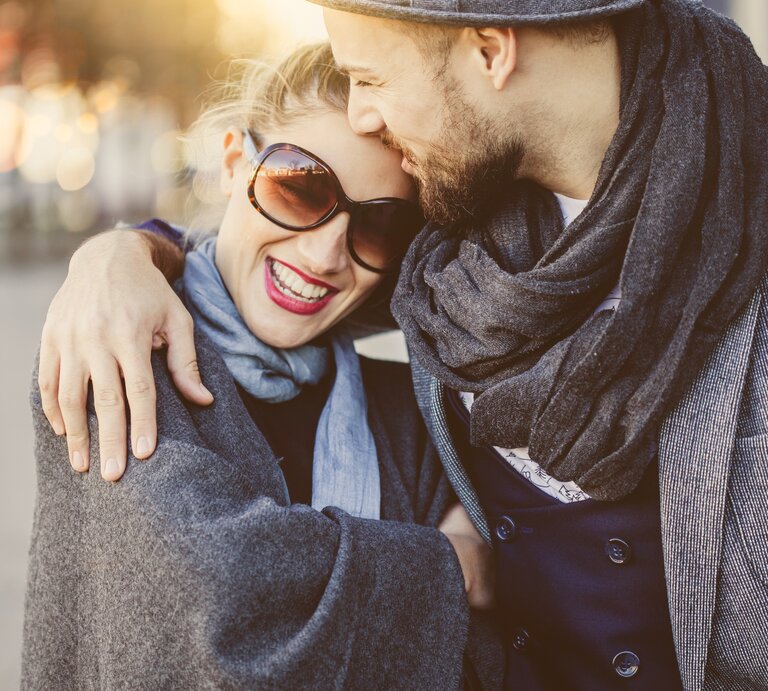 Ein junges Paar spaziert verliebt Arm in Arm, küssend und lachend  | © iStock/Jasmina007