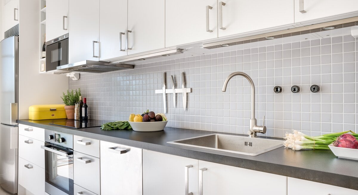 Moderne Küche mit einem eleganten und sauberen Design. Die Küchenzeile ist in Weiß gehalten, mit flächenbündigen Schränken und Edelstahlgriffen. 